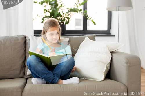 Image of little girl with diary sitting on sofa at home