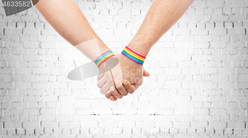 Image of hands of couple with gay pride rainbow wristbands