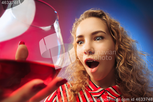 Image of The surprised young woman in party clothes posing with glass of wine.
