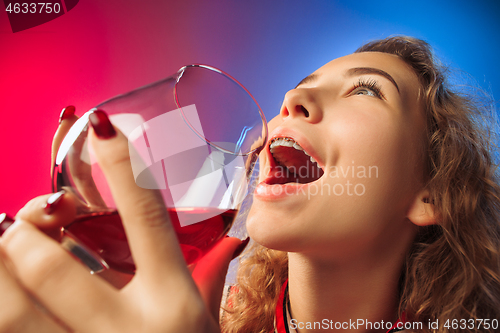 Image of The surprised young woman in party clothes posing with glass of wine.