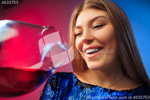 Image of The surprised young woman in party clothes posing with glass of wine.