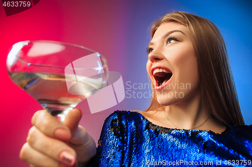 Image of The surprised young woman in party clothes posing with glass of wine.