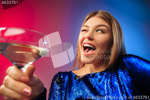 Image of The surprised young woman in party clothes posing with glass of wine.