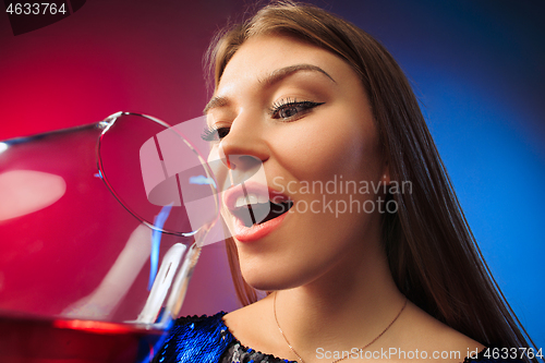 Image of The surprised young woman in party clothes posing with glass of wine.