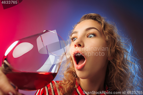 Image of The surprised young woman in party clothes posing with glass of wine.