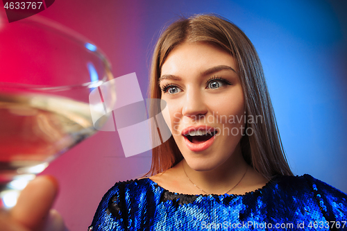 Image of The surprised young woman in party clothes posing with glass of wine.