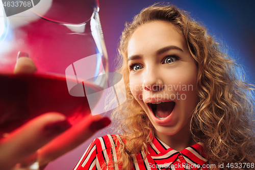 Image of The surprised young woman in party clothes posing with glass of wine.