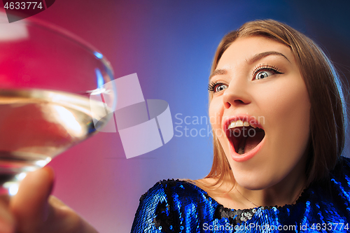 Image of The surprised young woman in party clothes posing with glass of wine.