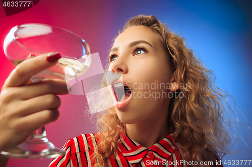Image of The surprised young woman in party clothes posing with glass of wine.