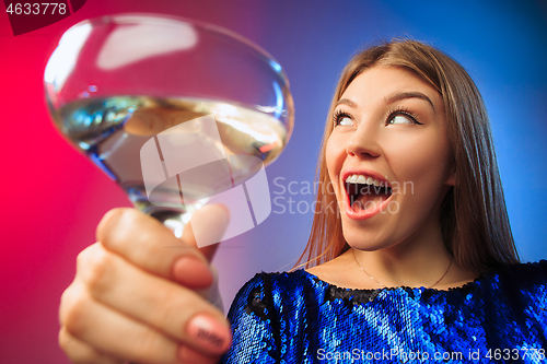 Image of The surprised young woman in party clothes posing with glass of wine.