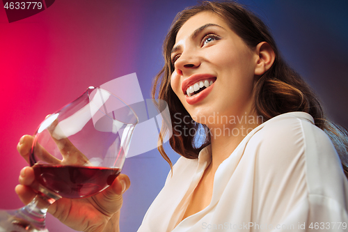 Image of The surprised young woman in party clothes posing with glass of wine.