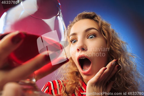 Image of The surprised young woman in party clothes posing with glass of wine.