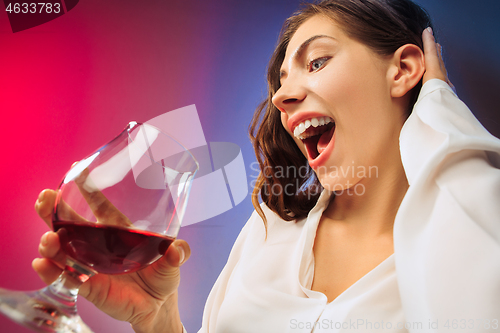 Image of The surprised young woman in party clothes posing with glass of wine.