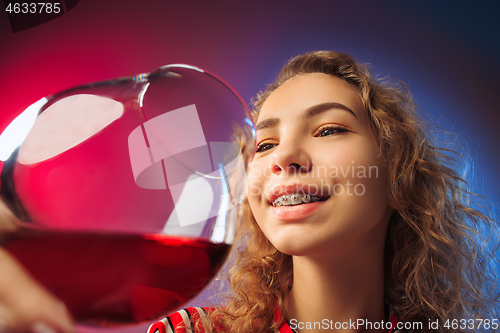 Image of The surprised young woman in party clothes posing with glass of wine.