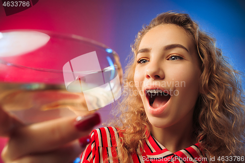 Image of The surprised young woman in party clothes posing with glass of wine.