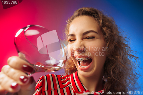 Image of The surprised young woman in party clothes posing with glass of wine.