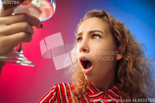 Image of The surprised young woman in party clothes posing with glass of wine.
