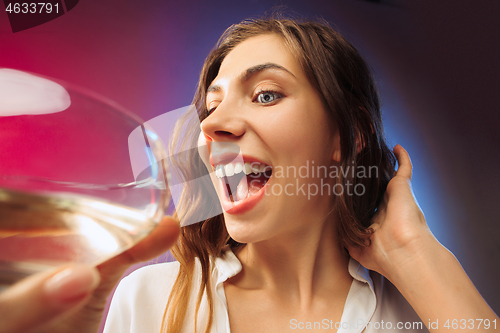 Image of The surprised young woman in party clothes posing with glass of wine.