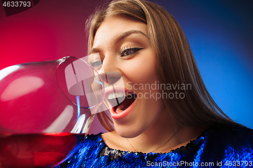 Image of The surprised young woman in party clothes posing with glass of wine.