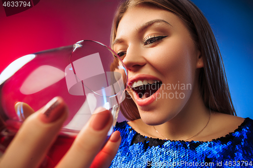 Image of The surprised young woman in party clothes posing with glass of wine.