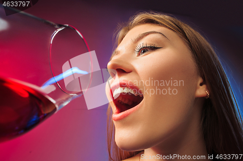 Image of The surprised young woman in party clothes posing with glass of wine.