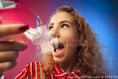 Image of The surprised young woman in party clothes posing with glass of wine.