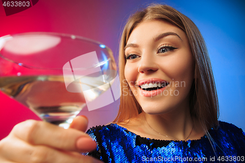 Image of The surprised young woman in party clothes posing with glass of wine.