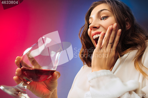 Image of The surprised young woman in party clothes posing with glass of wine.