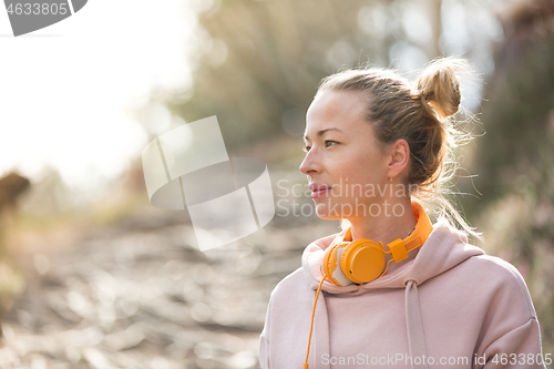 Image of Portrait of beautiful sports woman with hoodie and headphones during outdoors training session.