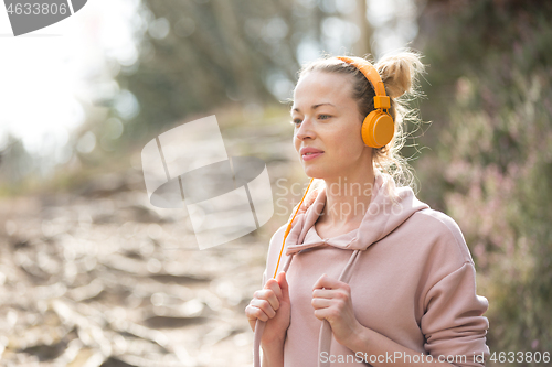 Image of Portrait of beautiful sports woman with hoodie and headphones during outdoors training session.