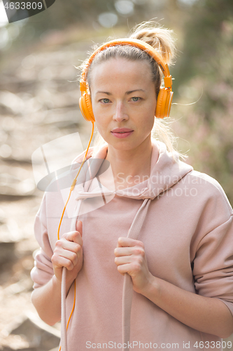 Image of Portrait of beautiful sports woman with hoodie and headphones during outdoors training session.