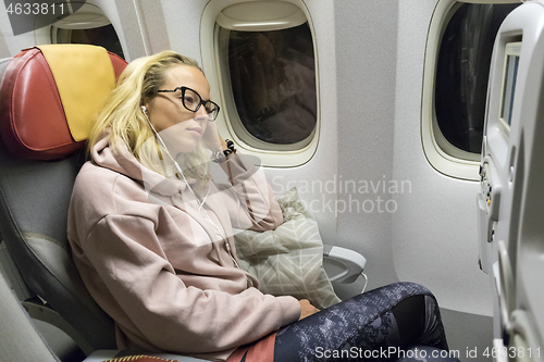 Image of Tired blonde casual caucasian lady napping on uncomfortable seat while traveling by airplane. Commercial transportation by planes.