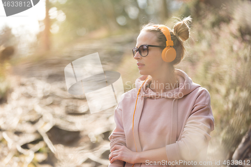 Image of Portrait of beautiful sports woman wearing sunglasses, hoodie and headphones during outdoors training session