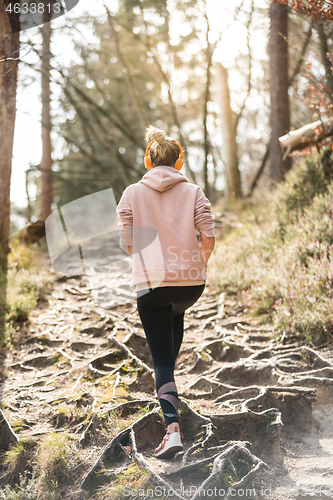 Image of Rear view of active sporty woman listening to the music while running in autumn fall forest. Female runner training outdoor. Healthy lifestyle image of young caucasian woman jogging outside