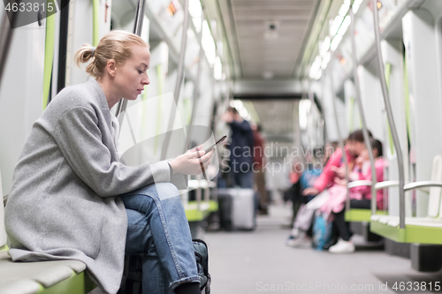 Image of Portrait of lovely girl typing message on mobile phone in almost empty public subway train. Staying at home and social distncing recomented due to corona virus pandemic outbreak