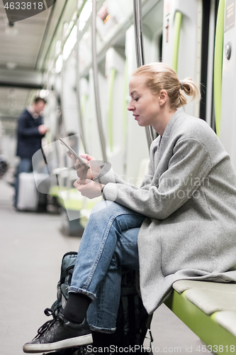 Image of Portrait of lovely girl typing message on mobile phone in almost empty public subway train. Staying at home and social distncing recomented due to corona virus pandemic outbreak