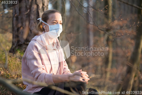 Image of Portrait of caucasian sporty woman wearing medical protection face mask while relaxing in nature and listening to music. Corona virus, or Covid-19, is spreading all over the world