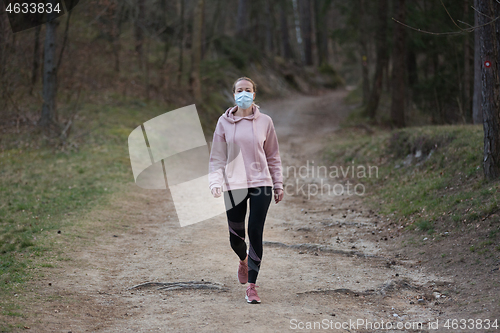 Image of Corona virus, or Covid-19, is spreading all over the world. Portrait of caucasian sporty woman wearing a medical protection face mask while walking in the forest. Corona virus.