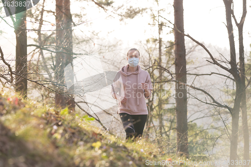 Image of Corona virus, or Covid-19, is spreading all over the world. Portrait of caucasian sporty woman wearing a medical protection face mask while running in nature.