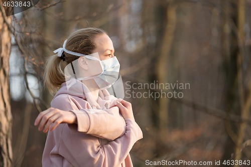 Image of Portrait of caucasian sporty woman wearing medical protection face mask while relaxing by stretching in forest. Corona virus, or Covid-19, is spreading all over the world
