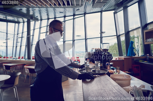 Image of waiter in a medical protective mask serves  the coffee in restau