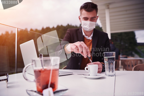 Image of man in restaurant drinking coffee wearing face mask