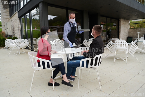 Image of Waiter with protective medical mask and gloves serving guest