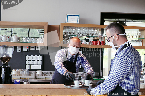 Image of waiter in a medical protective mask serves  the coffee in restau