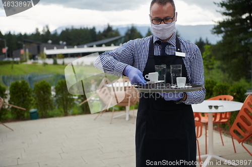 Image of waiter in a medical protective mask serves  the coffee in restau