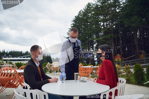 Image of Waiter with protective medical mask and gloves serving guest