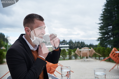 Image of funny man in restaurant drinking coffee wearing face mask