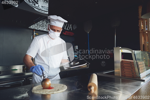 Image of chef  with protective coronavirus face mask preparing pizza