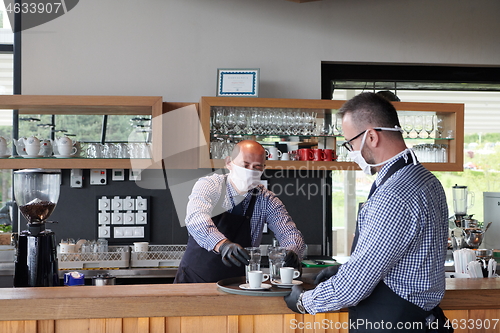 Image of waiter in a medical protective mask serves  the coffee in restau