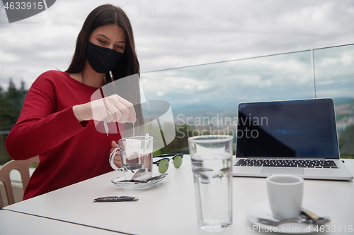 Image of woman in restaurant drinking tea wearingmedical  face mask